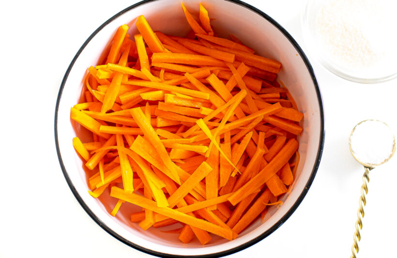 Julienned carrots in a bowl with pickling ingredients.