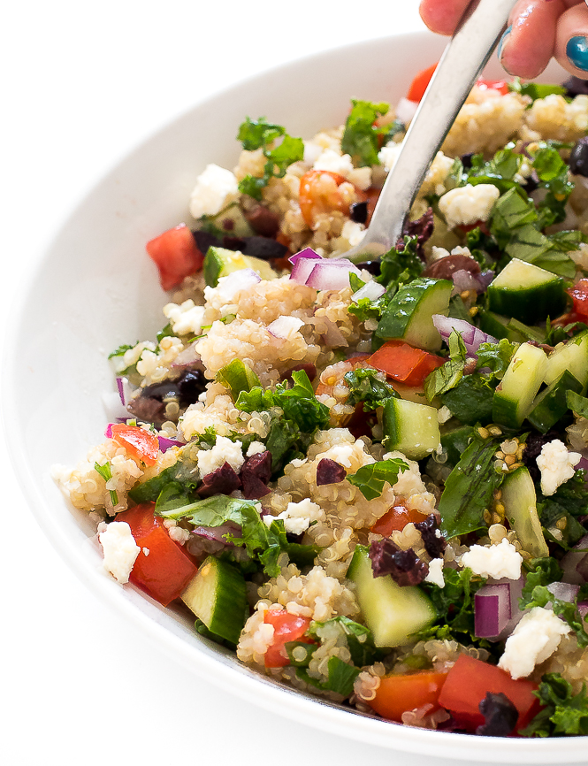 Kale Quinoa Salad | chefsavvy.com Hand holding spoon taking a scoop of the Greek Kale Quinoa Salad from a white bowl.