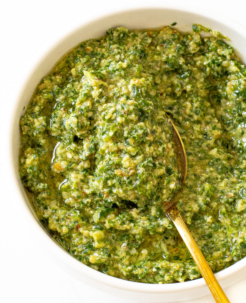 Kale pesto served in a white bowl with a golden spoon.