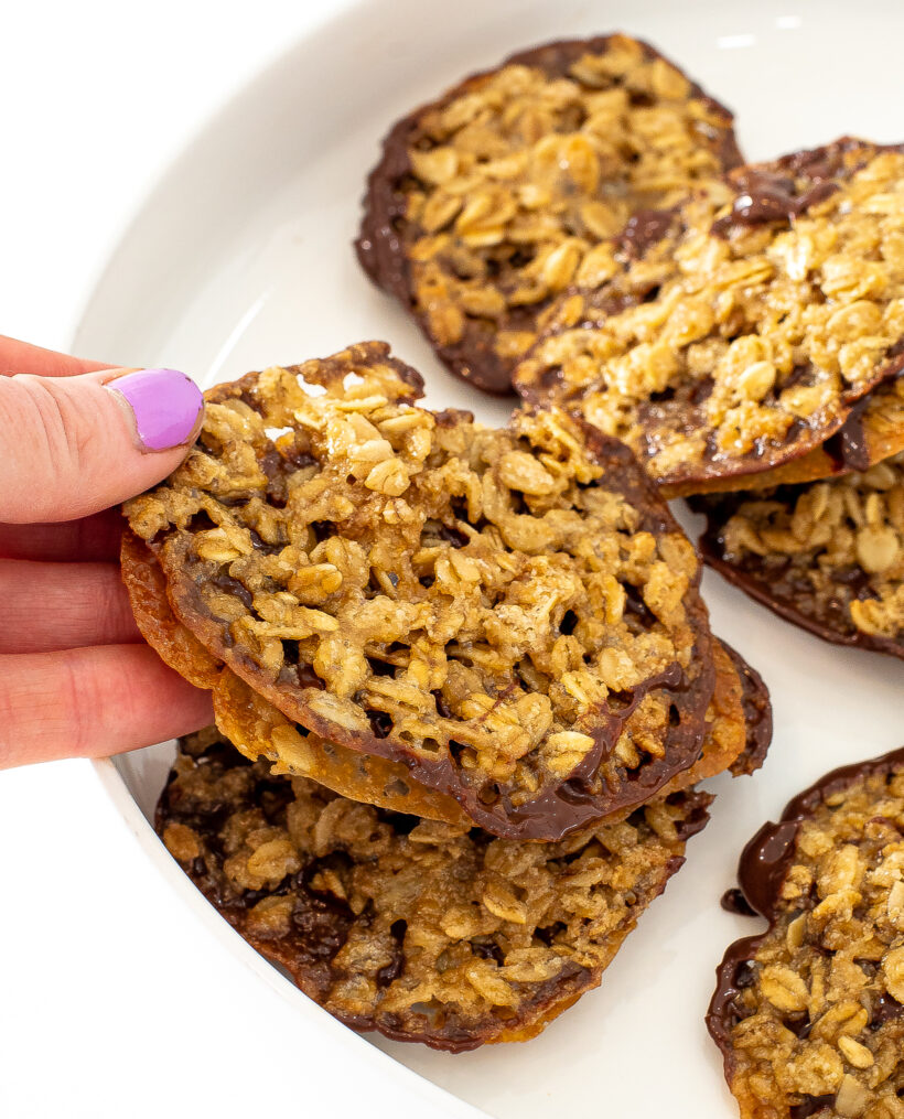 Hand holding a oatmeal lace sandwich cookie with more in the background.