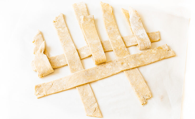 Pie crust dough being weaved into a lattice top.