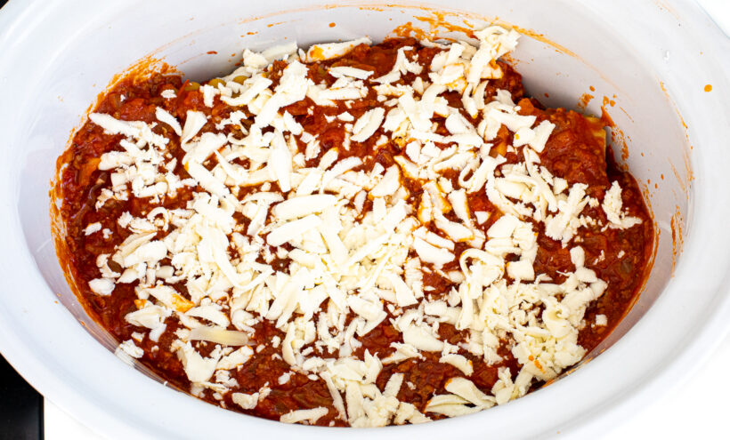 Lasagna ingredients layered with cheese on top in a white slow cooker liner.