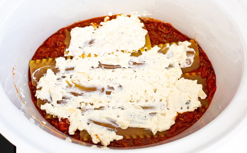 Lasagna ingredients layered in a white slow cooker liner. 