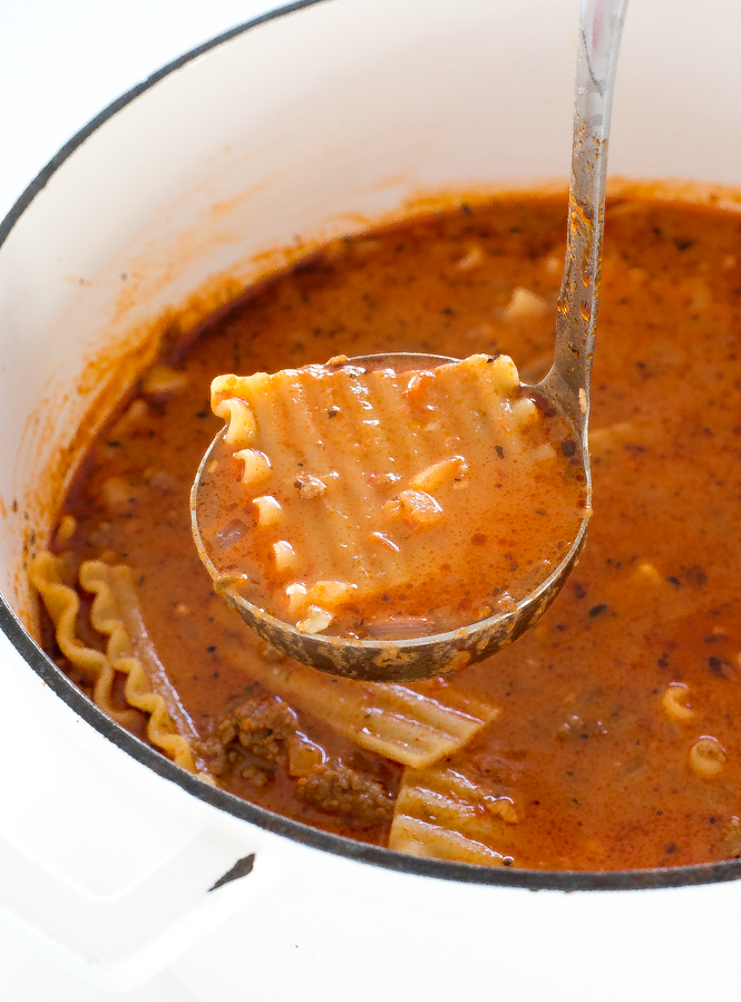 ladle scooping soup with noodles out of white pot