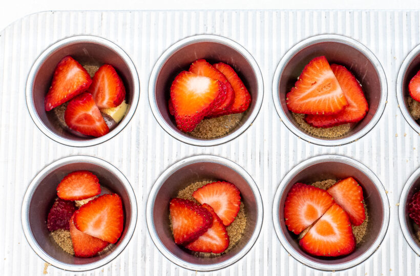 Muffin tin with layer of strawberries at the bottom of each cavity. 