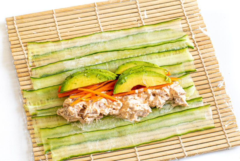 Assembling the cucumber sushi rolls on a sushi mat lined with plastic wrap.