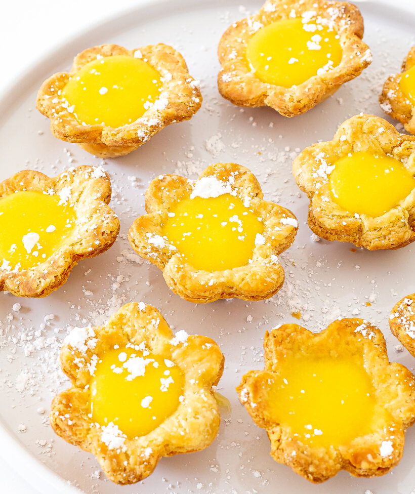Mini lemon flower tarts filled with lemon curd and served on a white plate.