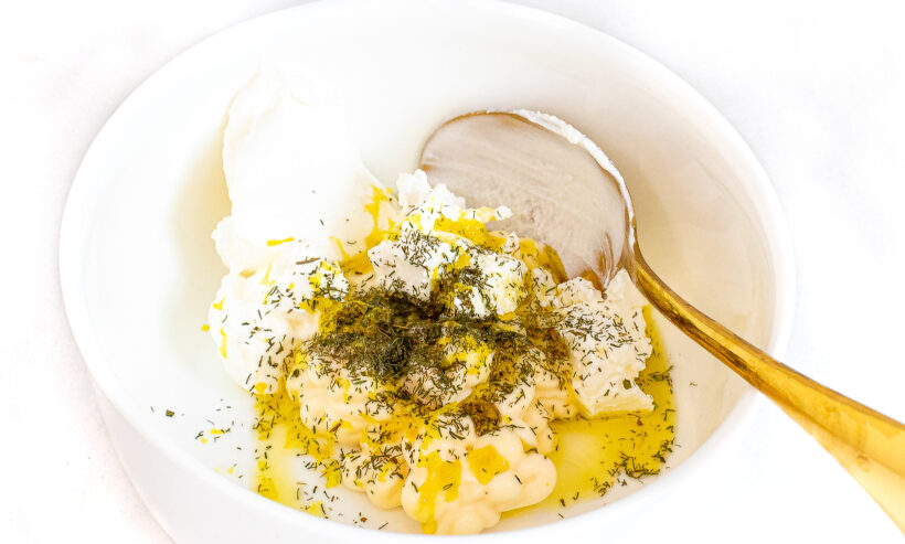Ingredients for lemon dill sauce in a white bowl with a gold spoon.