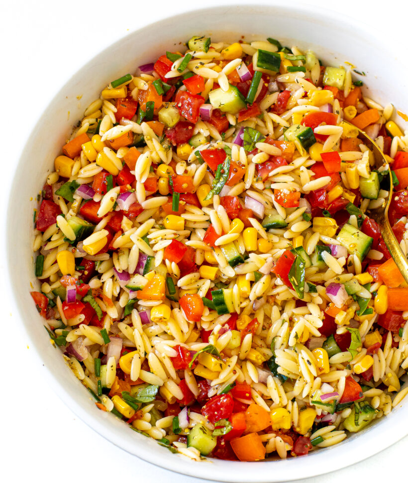 Orzo pasta salad with lots of veggies served in a white serving bowl. 