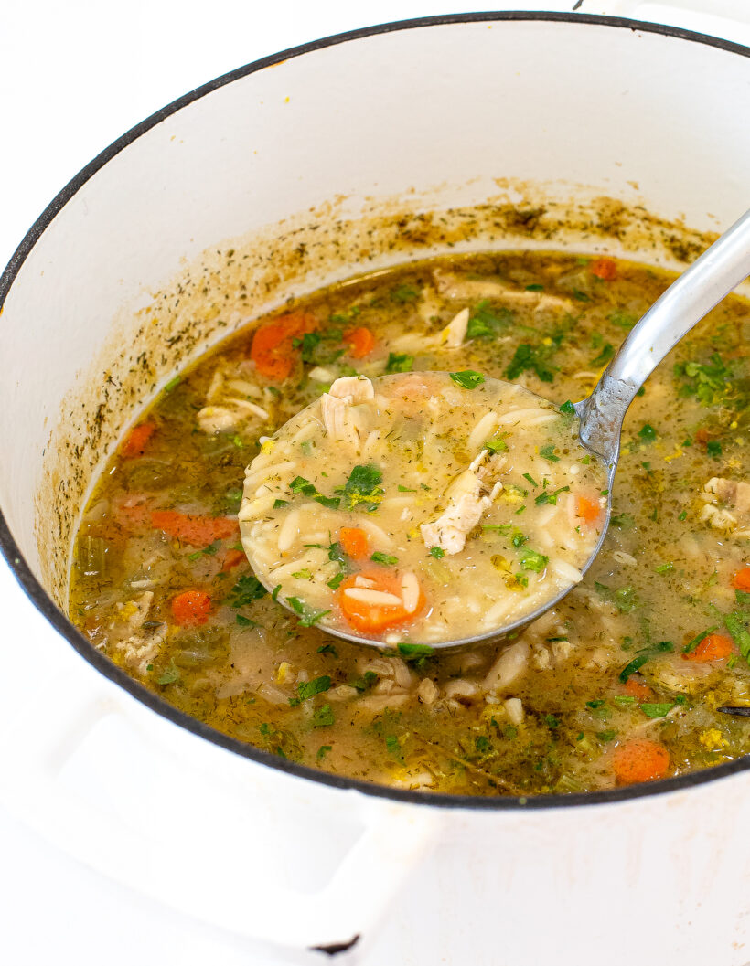 Large pot of chicken orzo soup with a ladle scooping out a portion. 