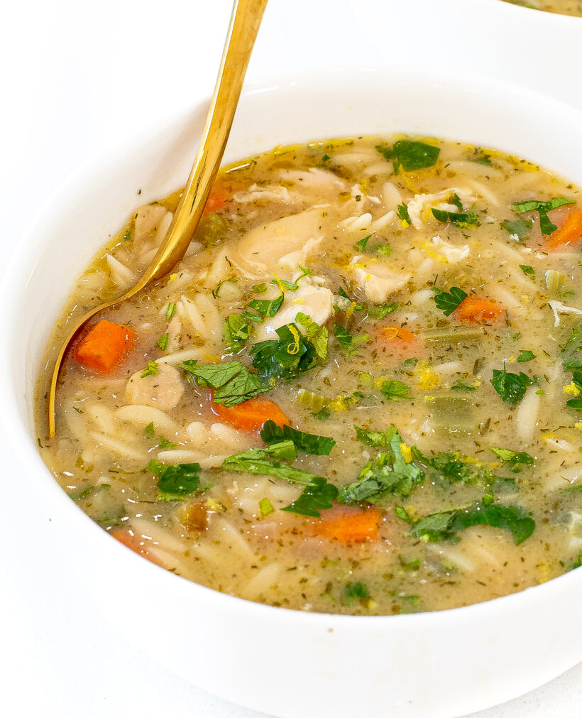 Bowl of lemon chicken orzo soup, garnished with parsley with a gold spoon. 
