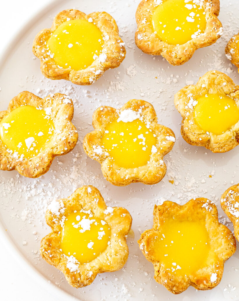 Overhead shot of mini lemon flower tarts on a white surface and dusted with powder sugar.