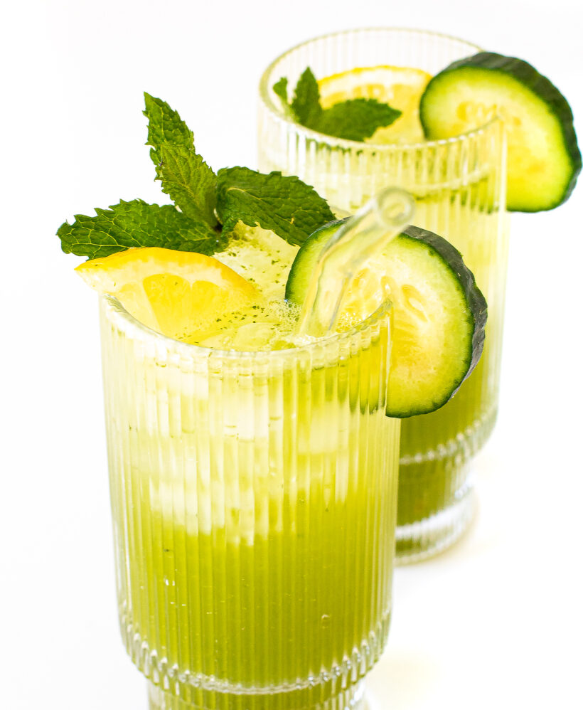 Two glasses of cucumber mint lemonade with garnishes of cucumber, lemon and mint.