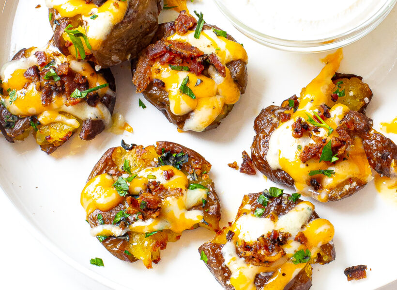 Loaded smashed potatoes with melted cheese, bacon and parsley on top.