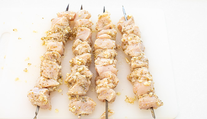 Raw chicken on skewers on a cutting board.