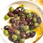 Marinated olives over whipped ricotta in a white bowl.