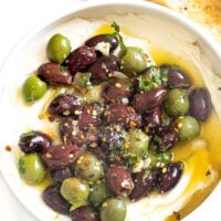 Marinated olives over whipped ricotta in a white bowl.