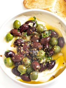Marinated olives over whipped ricotta in a white bowl.
