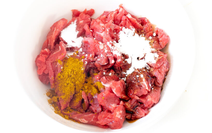 Sliced flank steak in a bowl with marinade ingredients.