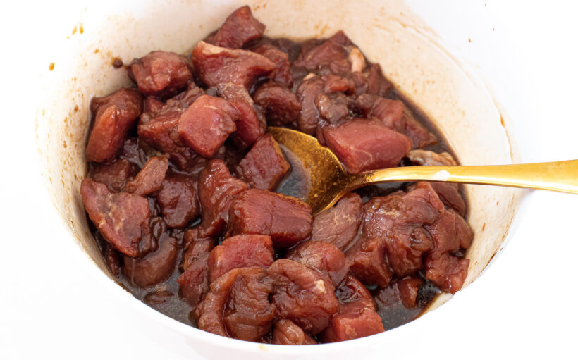 Cubed pork being marinated in a white bowl.