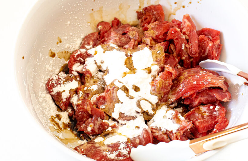 tossing cornstarch, soy sauce and flank steak in white bowl