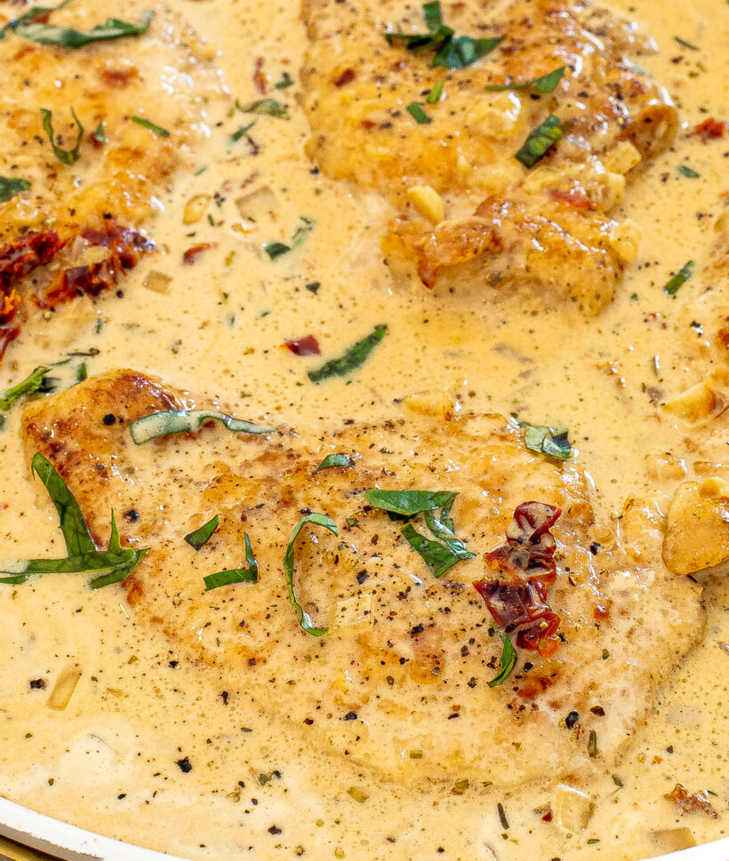 Close up shot of a piece of chicken in a creamy sauce with more chicken around it.