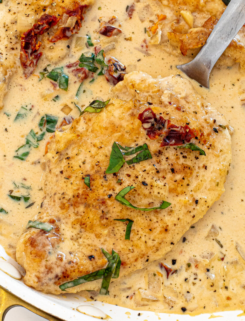 Spatula taking a piece of chicken from the sauce in a skillet.