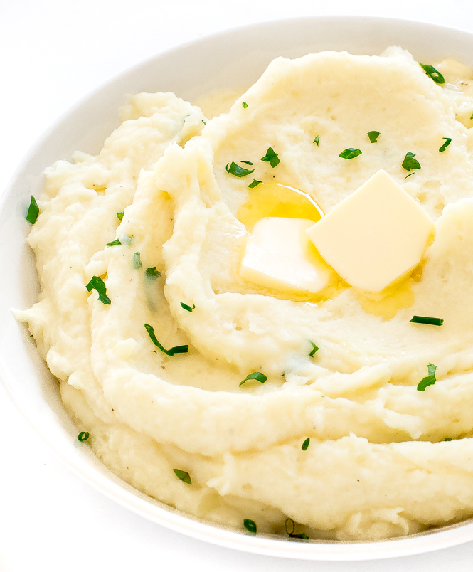 close up shot of mashed potatoes in a white bowl topped with butter and parsley