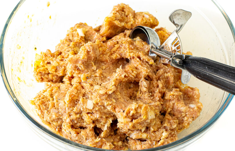 Meatball mixture with a cookie scoop in a mixing bowl.