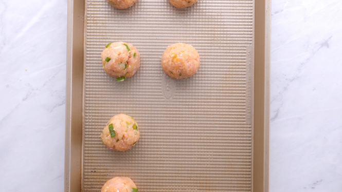 Meatballs lined up on a baking sheet before being baked. 