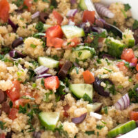 Close up of Mediterranean quinoa with a spoon in a white bowl.