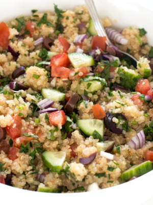 Close up of Mediterranean quinoa with a spoon in a white bowl.