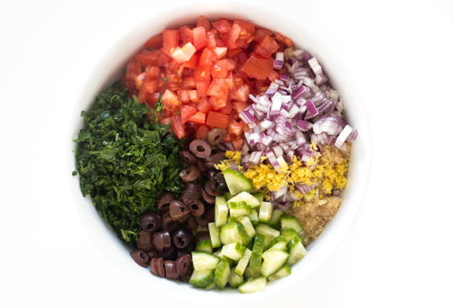 Top shot of chopped vegetables, olives, and herbs arranged in a white bowl.