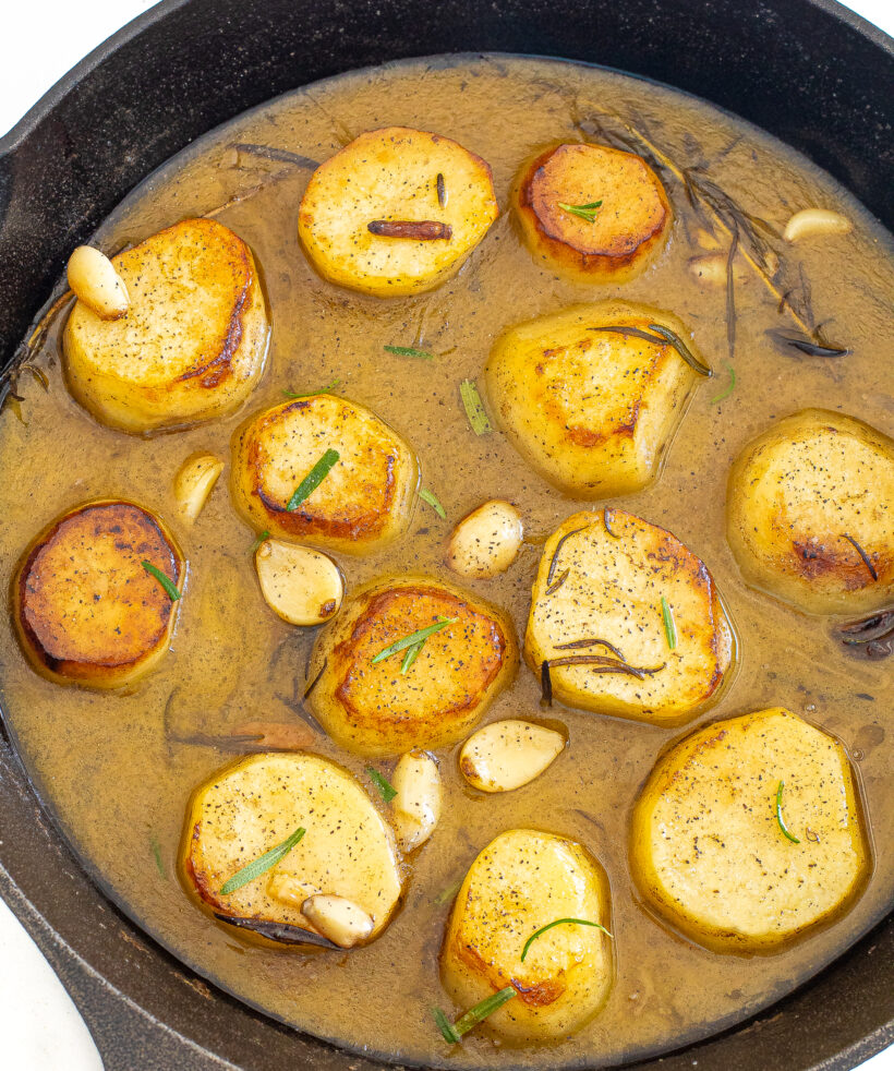 Melting potatoes in a skillet with rosemary and gravy. 