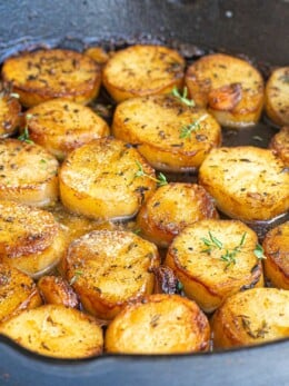 Golden-brown melting potatoes seared in a skillet with herbs and garlic.
