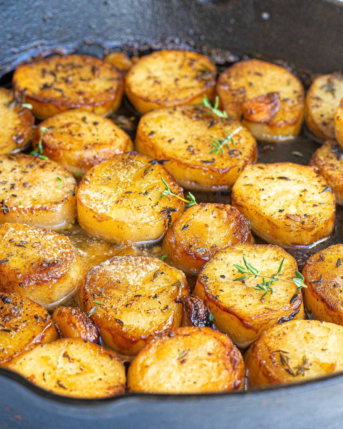 Golden-brown melting potatoes seared in a skillet with herbs and garlic.