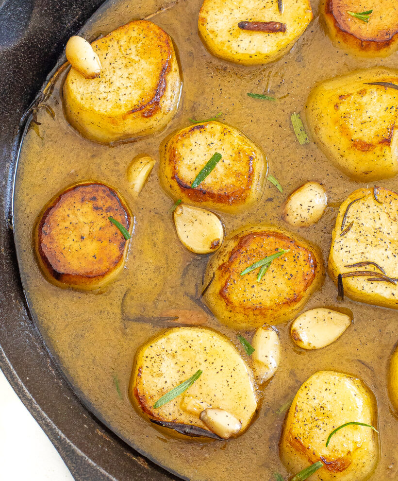 Melting potatoes in a skillet with garlic cloves, rosemary and a gravy sauce. 