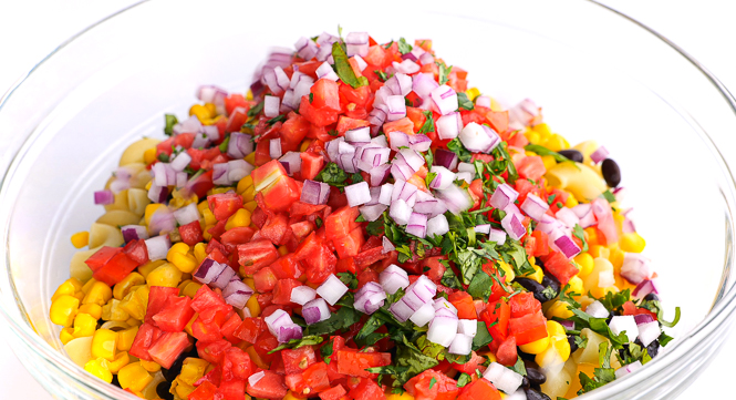 Mexican pasta salad ingredients in large clear bowl.