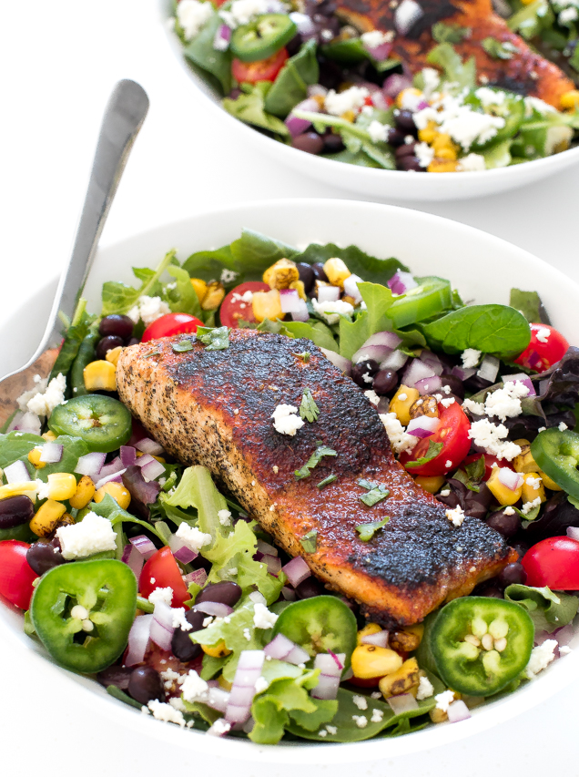Salad in a white bowl with jalapenos, tomatoes, corn, onions and a salmon filet on top.