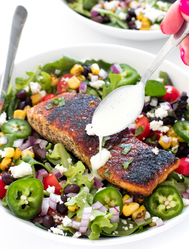 Hand drizzling a white dressing on top of the salmon salad.