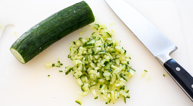 Cucumbers finely chopped on a white cutting board.