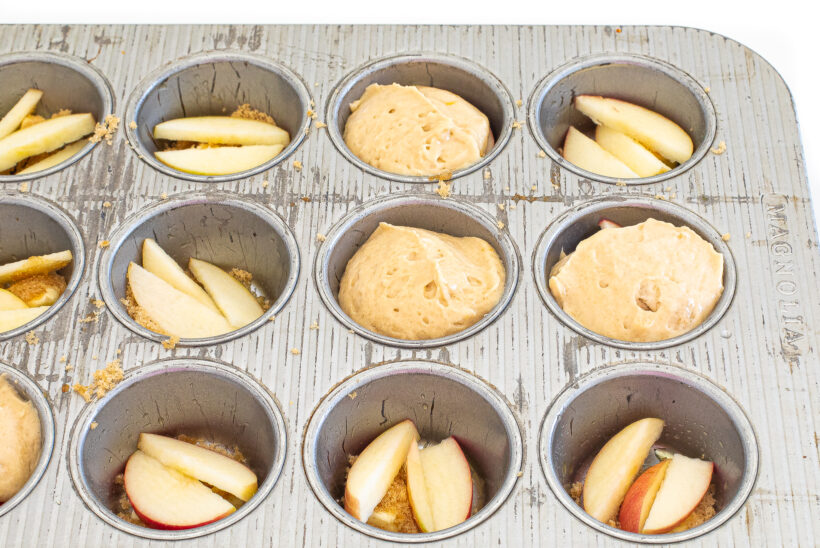 Filling the muffin tin with apples and cake batter on top.