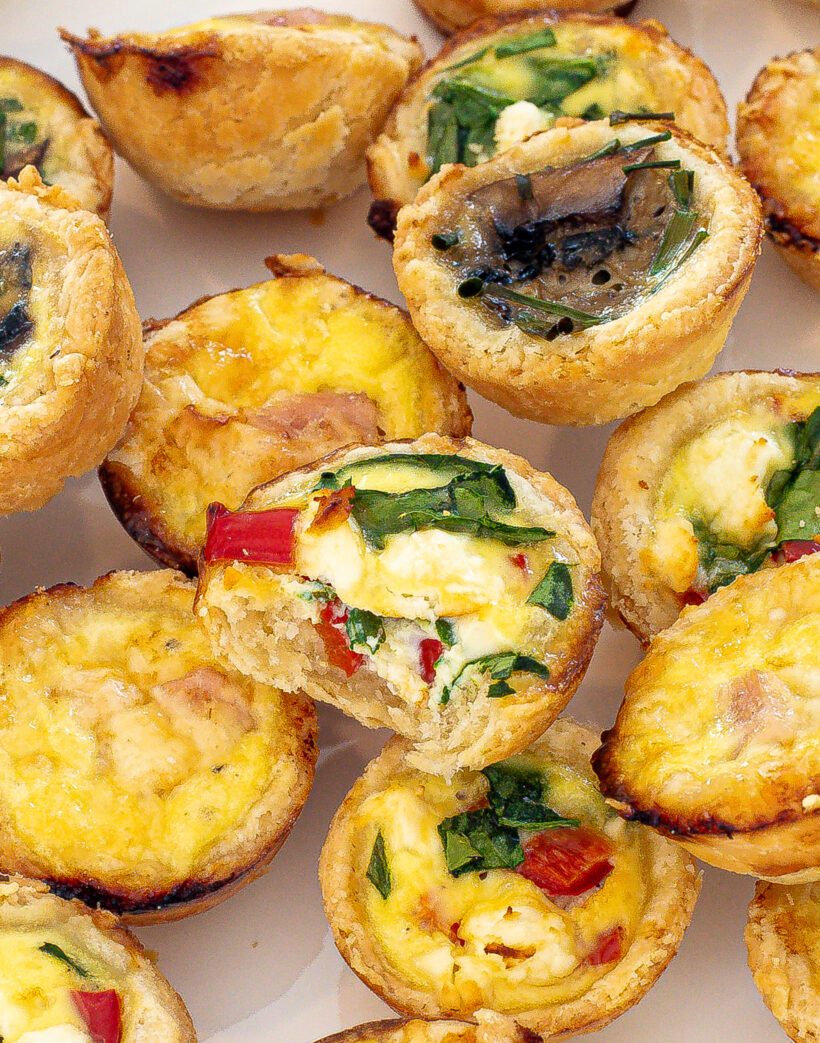 Mini quiches on a plate with one quiche missing a bite