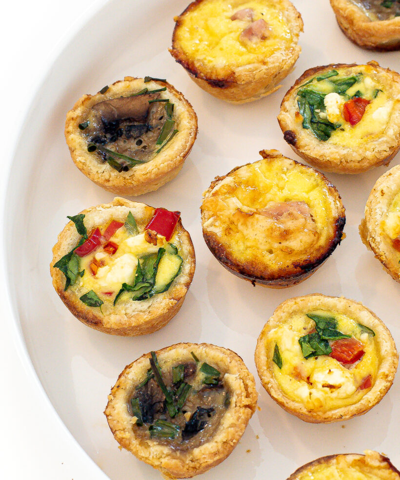 Mini quiche 3 ways lined up on a white serving tray.