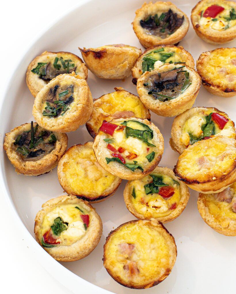 Mini quiches on a white plate with some quiche stacked on top of others.