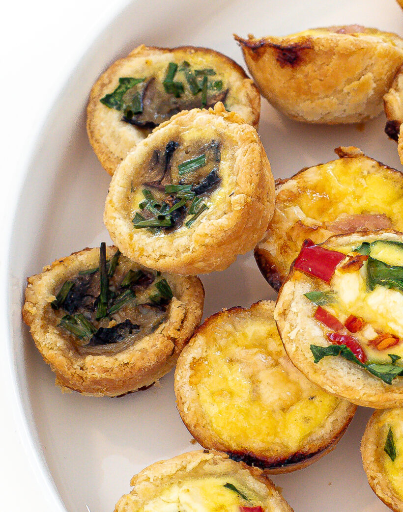 Mini quiches stacked on top of each other on a white plate.