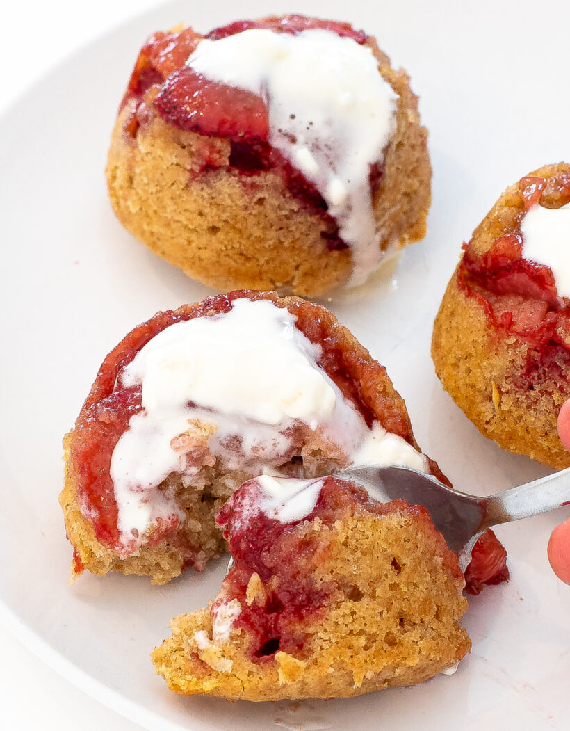 Spoon holding a bite of cake next to the rest of the cake on a white plate. 