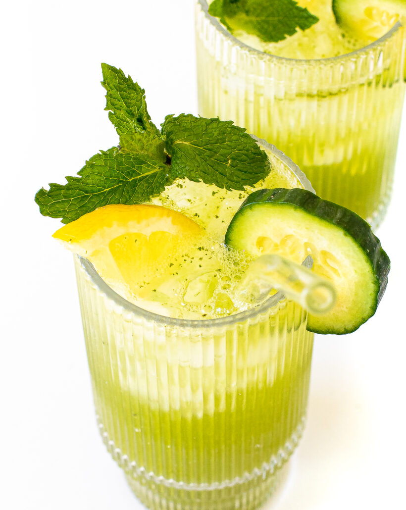 Two glasses of mini cucumber lemonade garnished with cucumber, lemon and mint.