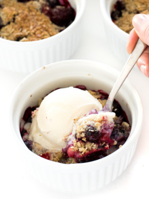 front view of mixed berry crisp in white dish with ice cream and spoon