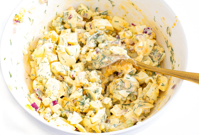The best egg salad being mixed together in a large white bowl. 